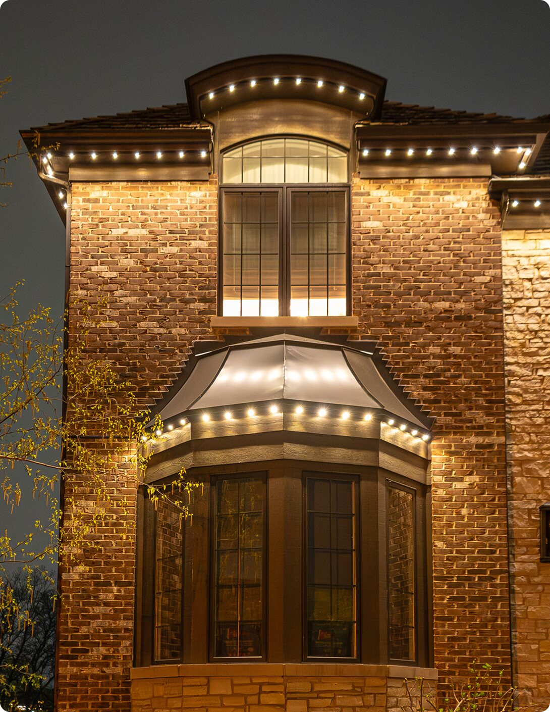 Forever Lighting permanent outdoor lighting in warm white on a brick home — app-controlled architectural LEDs