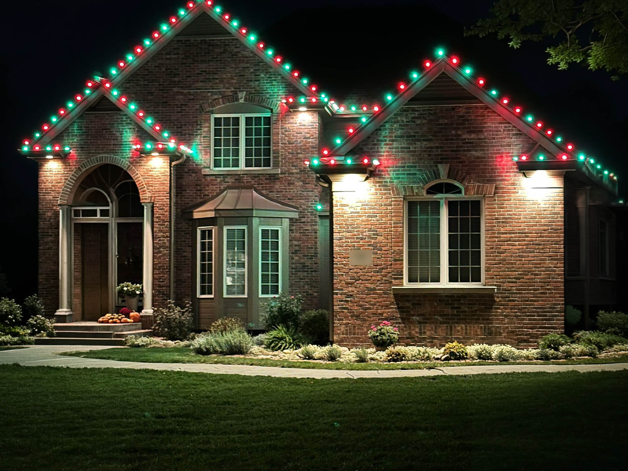 Brick Tudor-style home with red and green holiday lighting along the roofline