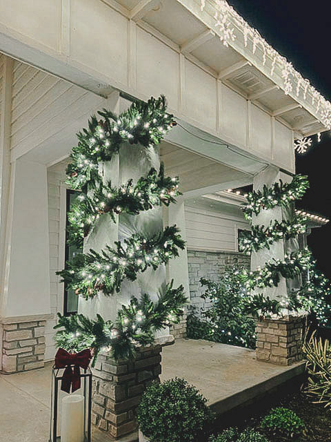Close-up of garland-wrapped porch columns with icicle lighting and a velvet bow